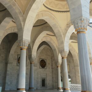 Elegant arches and marble columns defining the grand architecture of a mosque interior on a sunny day.