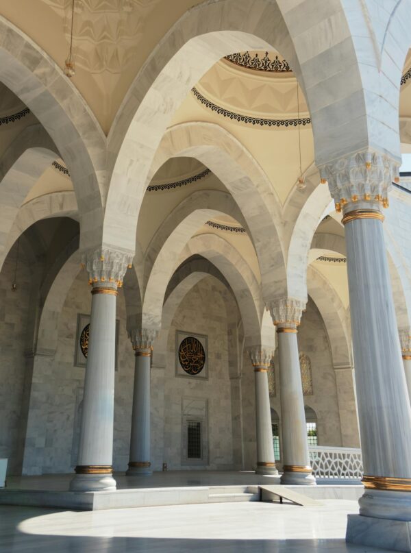 Elegant arches and marble columns defining the grand architecture of a mosque interior on a sunny day.